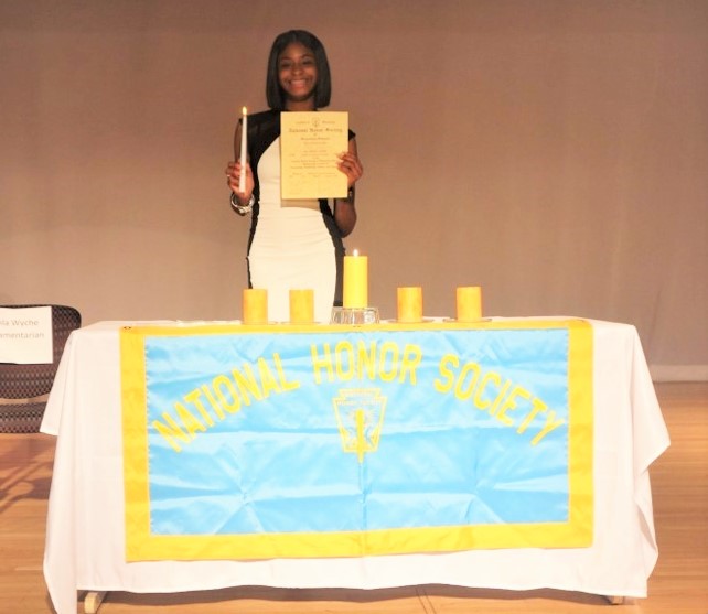 Person holding a document in front of a table with a National Honor Society banner, candles.