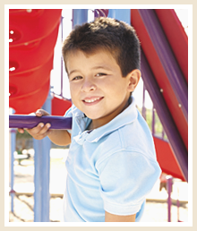 a young boy stands in front of playground equipment and smiles