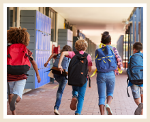 5 students with backpacks on run down a locker-lined hallway