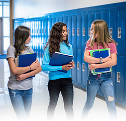 three students holding notebooks and walking down a hallway in front of blue lockers