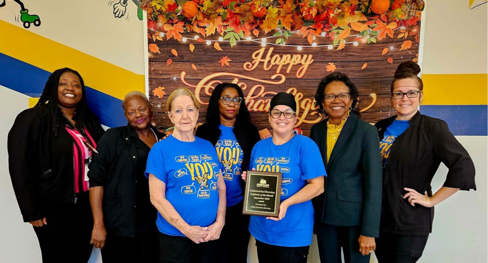 Seven women standing in together and posing with a plaque.