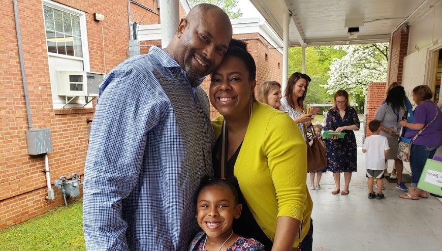 tWO PARENTS with their child smiling in an outdoor school hallway.