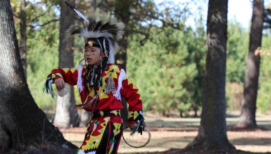 A boy dressed in native regalia dancing in a park.