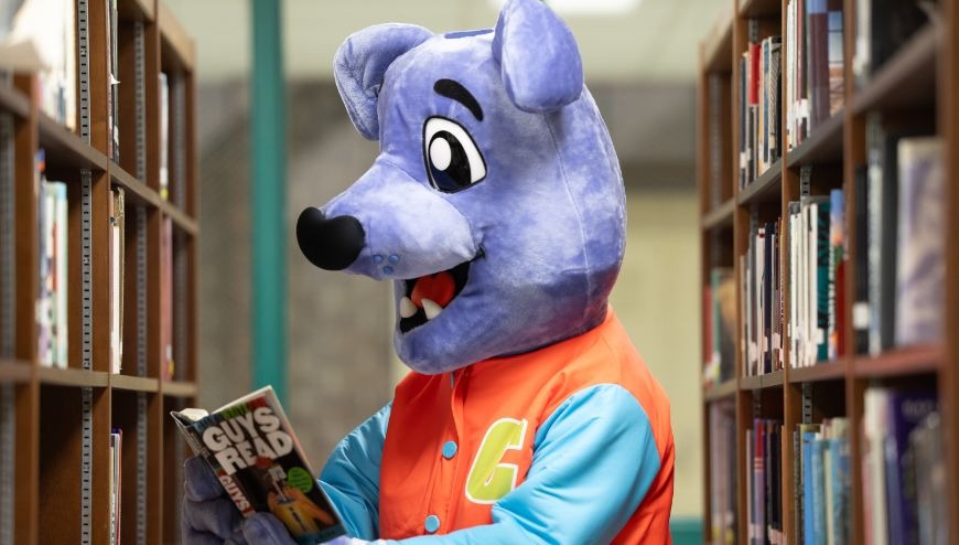 Image of mascot Cooper reading in a library