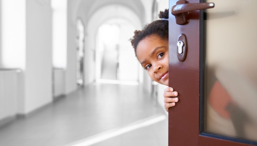 image of child peeking behind classroom door