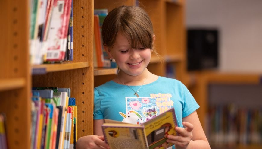 Elementary student reading a book in library