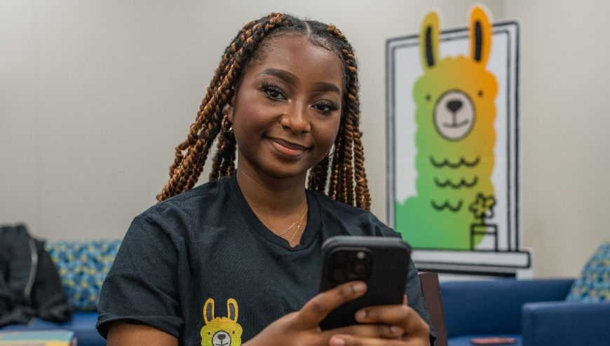 Girl holding cellphone. A cartoon Llama poster is on the wall. 