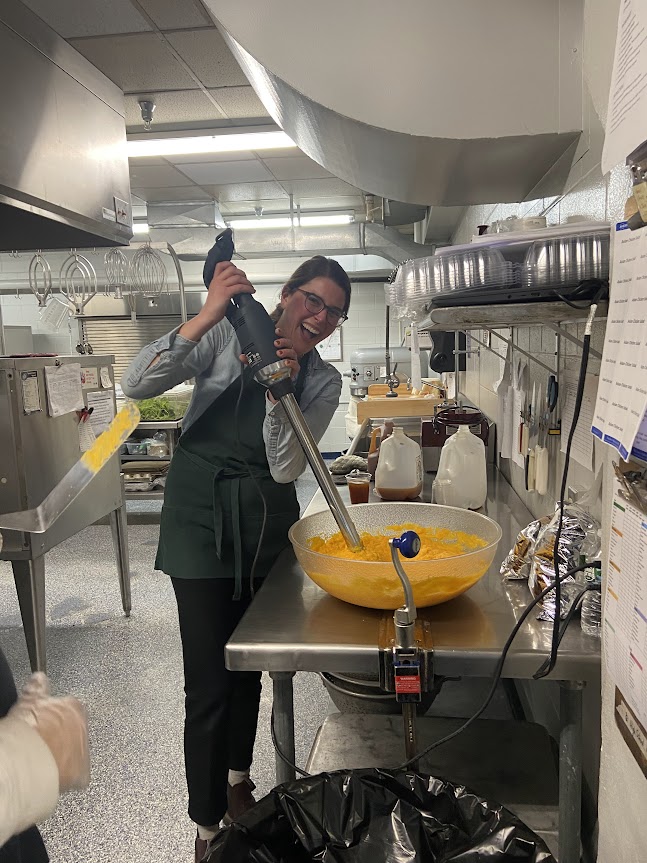 A happy chef stirring a huge batch of squash with an industrial mixing device.