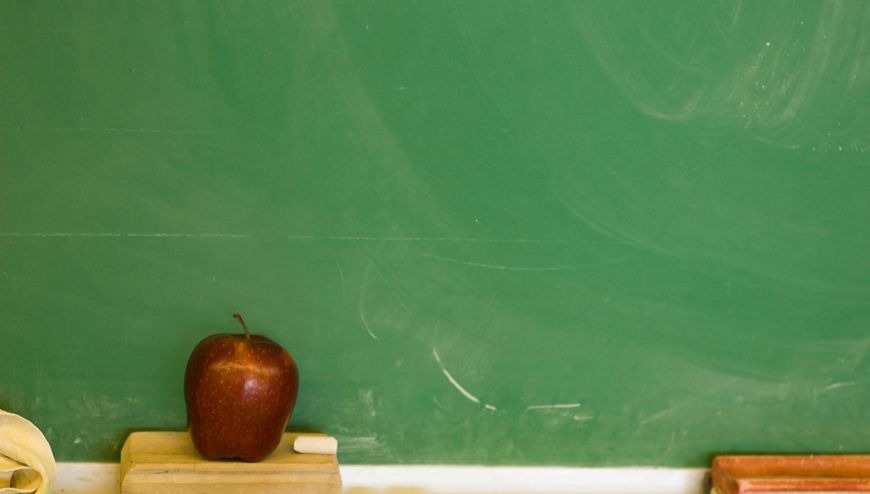 Red apple sitting in front of a green chalkboard