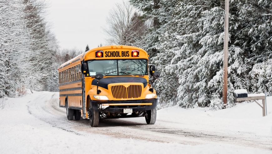 yellow school bus driving on a snowy road. 