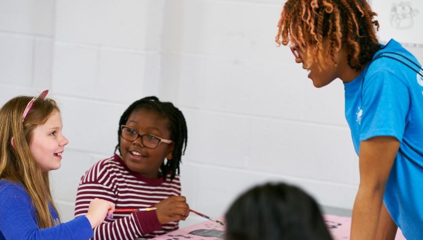 Two children smiling and painting with a teacher