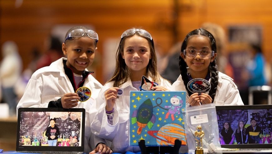 Students in white lab coats holding STEM patches