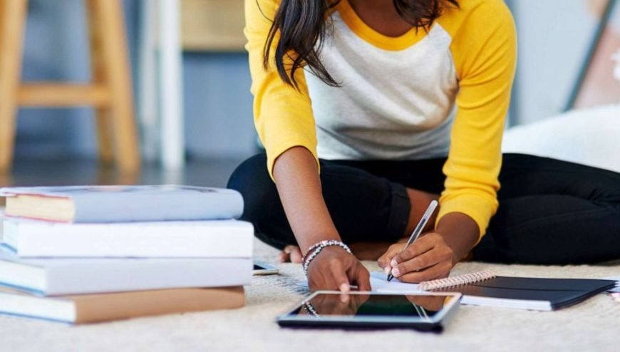 Student sitting on the floor with file of books next to her