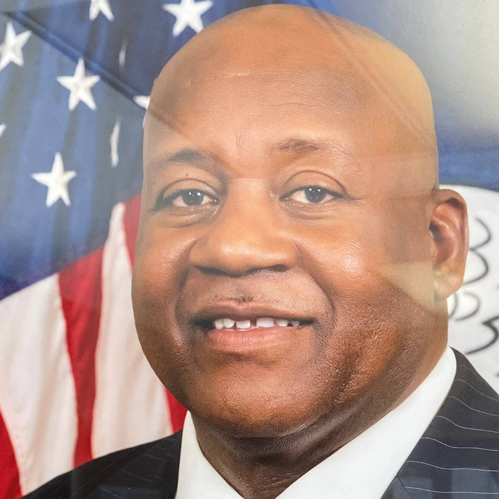 A black man in a suit and tie standing proudly in front of an American flag.