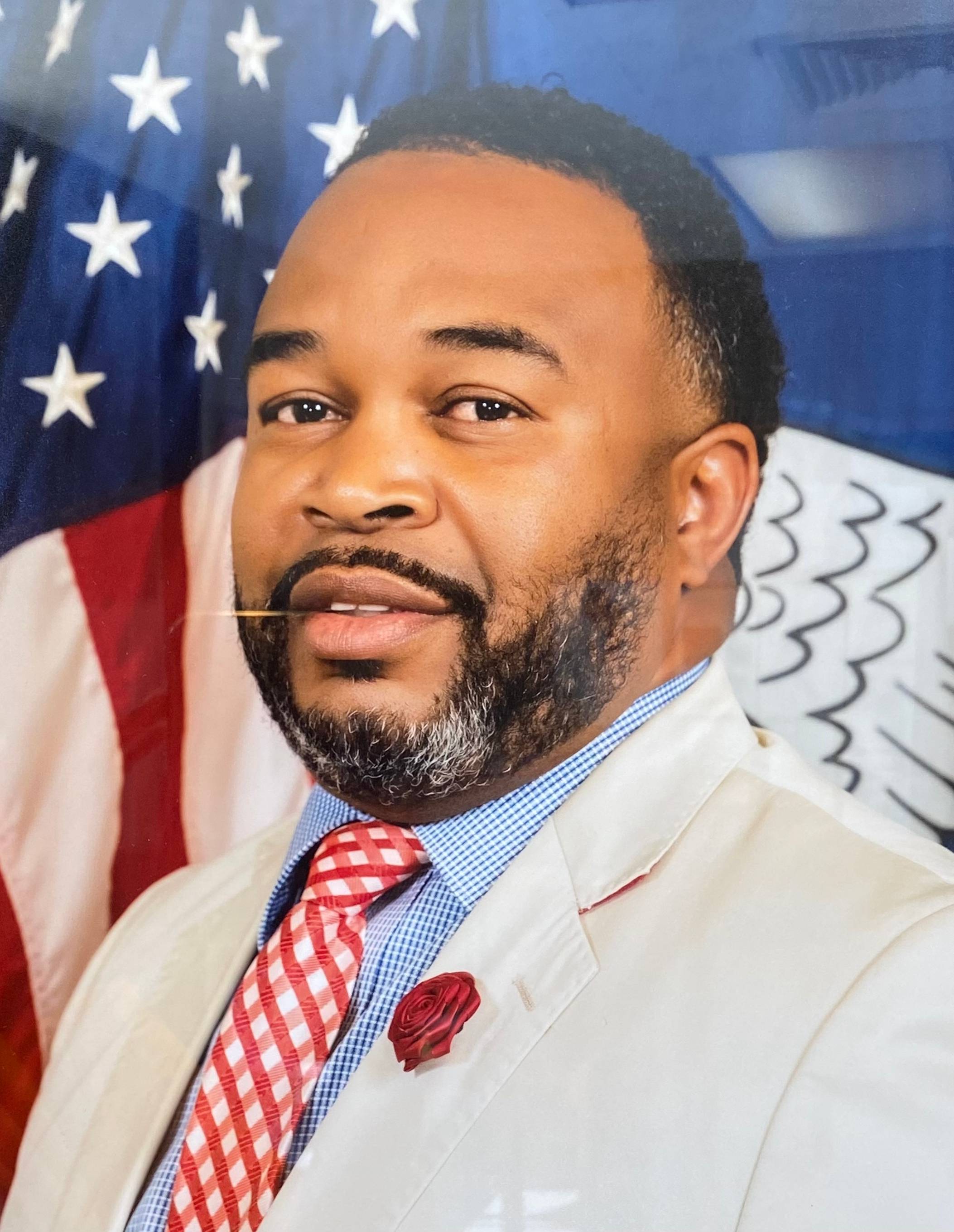 A black man in a suit and tie standing proudly in front of an American flag.