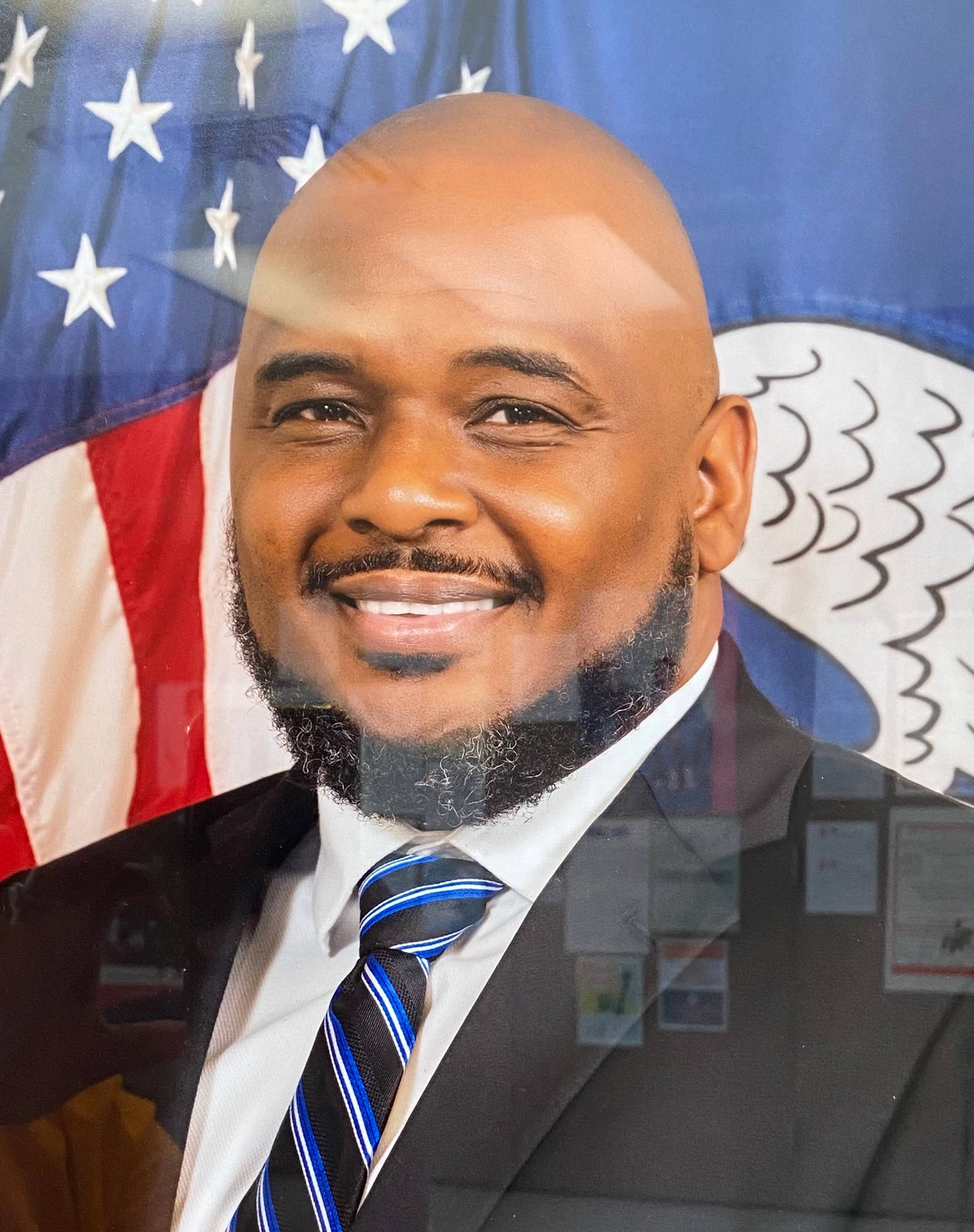 Man in suit smiling in front of American flag.