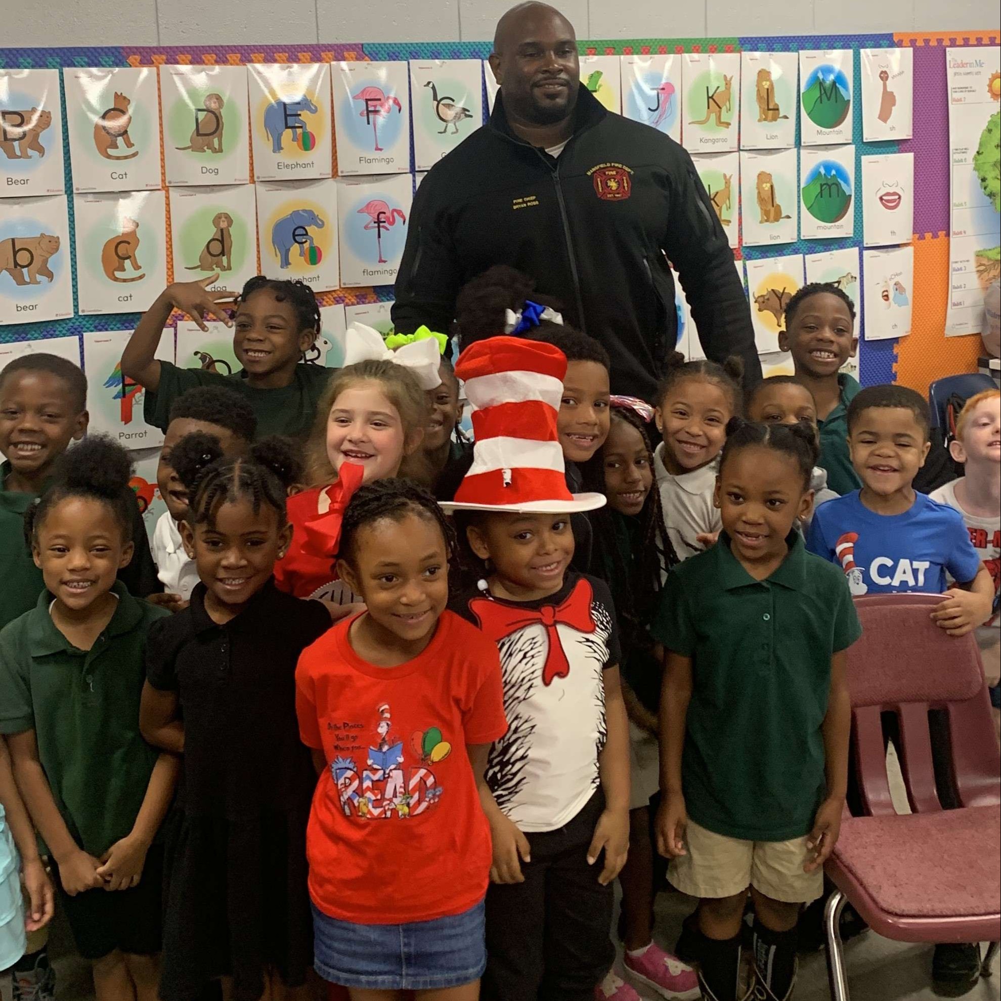 A man in a hat standing with a group of children in a classroom.