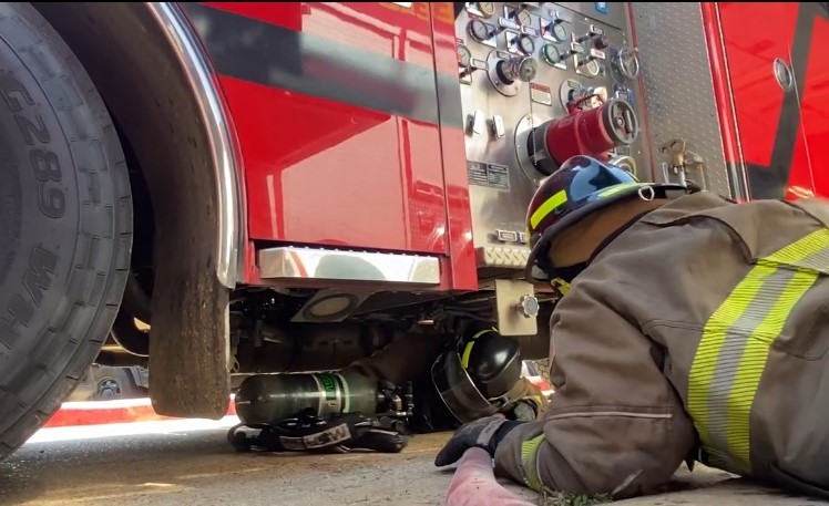 A firefighter lying next to a fire truck.