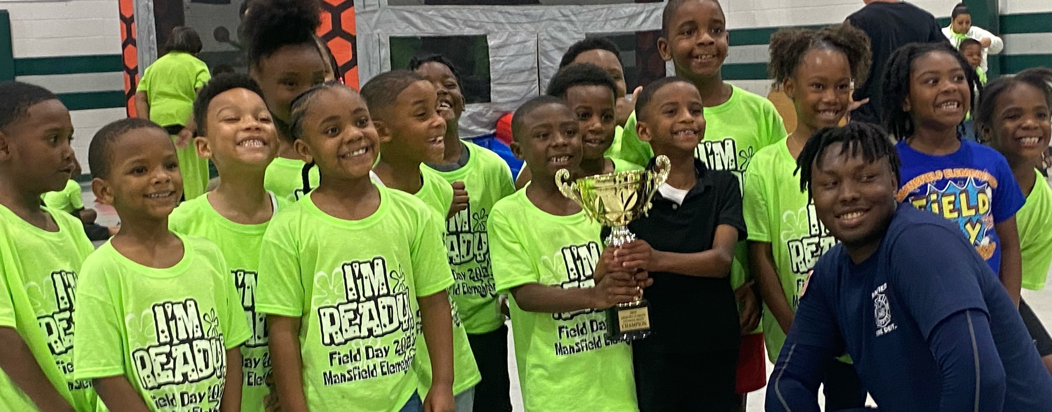 Children in matching green shirts smiling for a group picture.