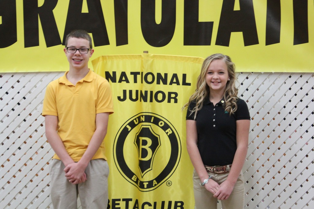 Two young people smiling in front of a banner that says congratulations.