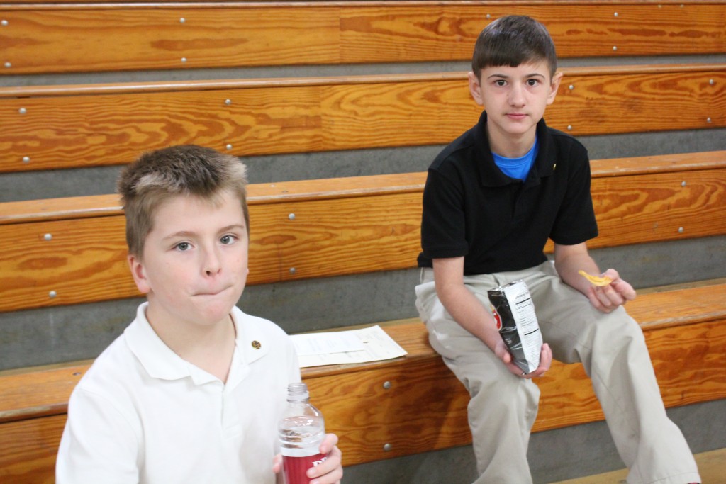 Two boys sitting on bleachers holding drinks.