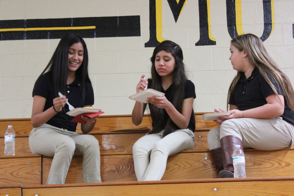 Three girls enjoying snacks while seated on bleachers.