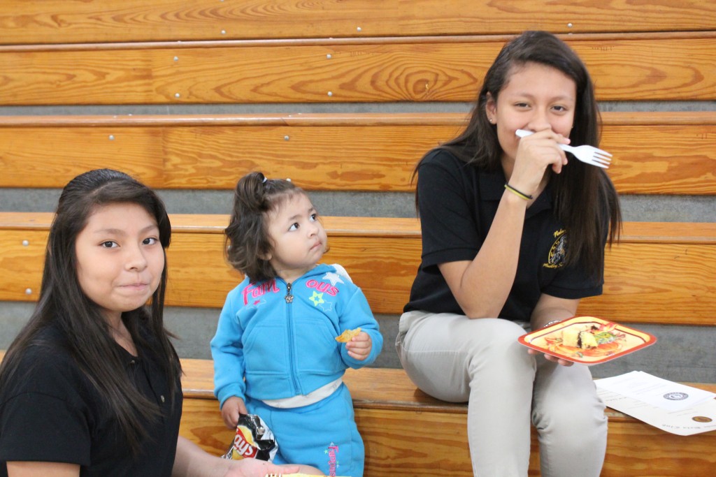 Two women and a child enjoying pizza on a bench in the park.