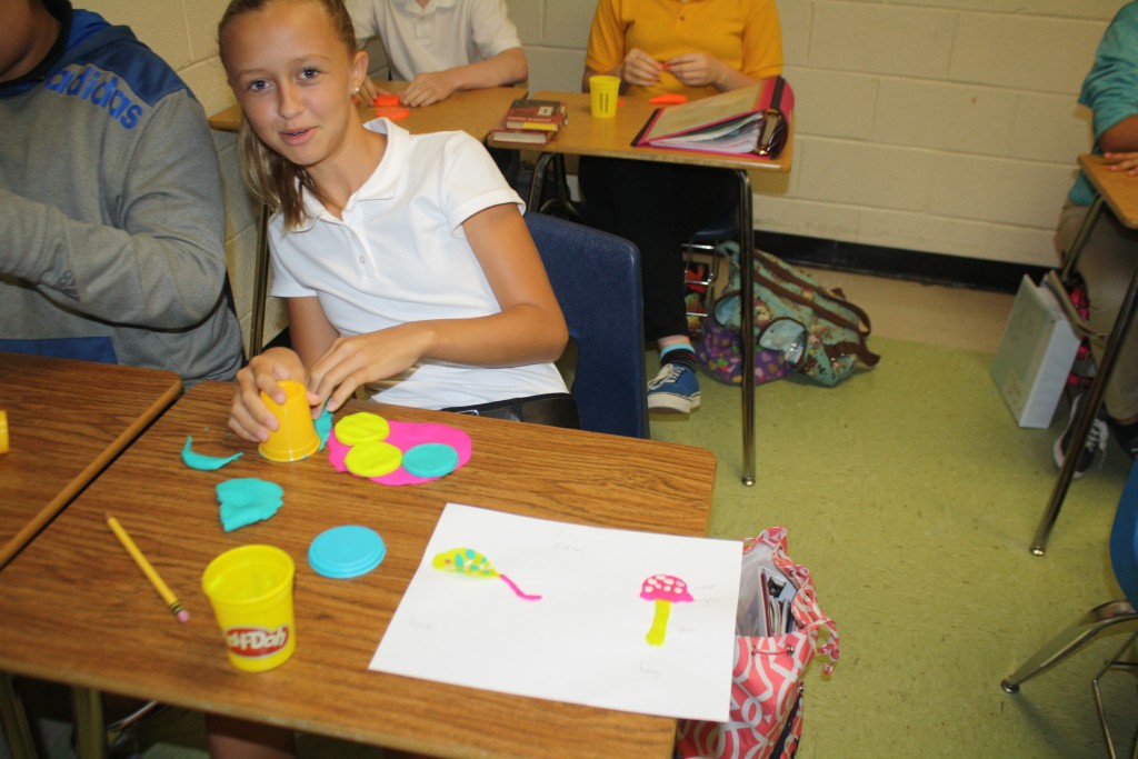 A girl sitting at a desk with a cup of yellow paint.