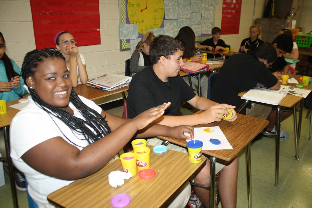  group of students sitting at a table with colorful toys and cups.