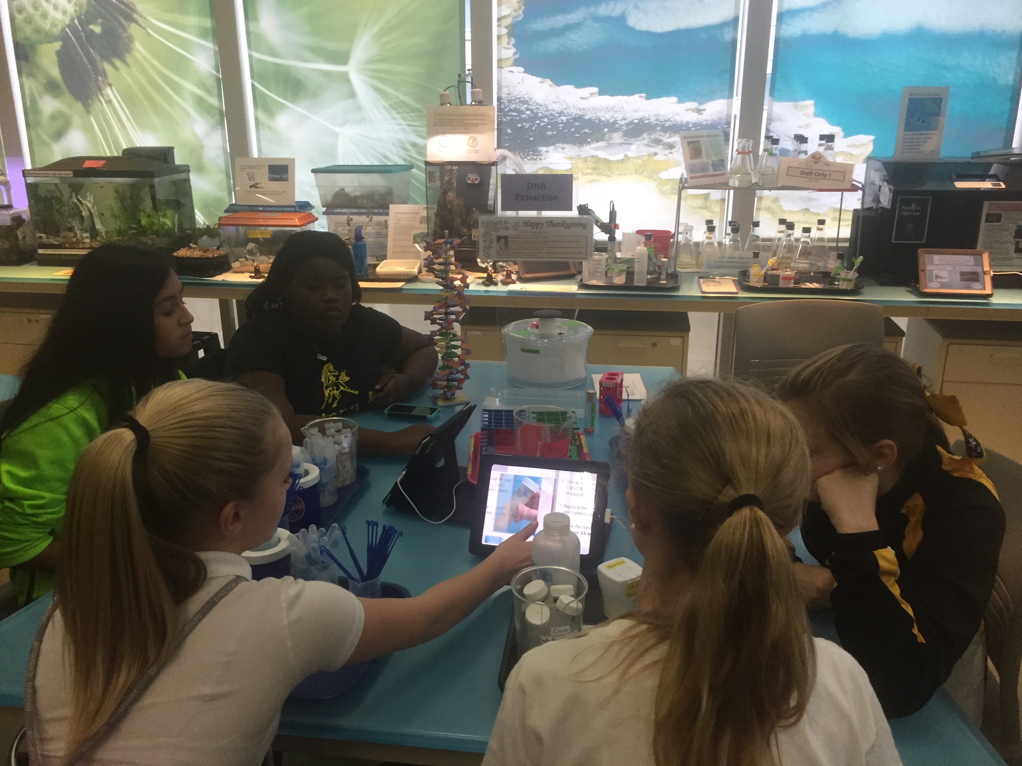 Several girls sitting at a table, looking at a tablet.