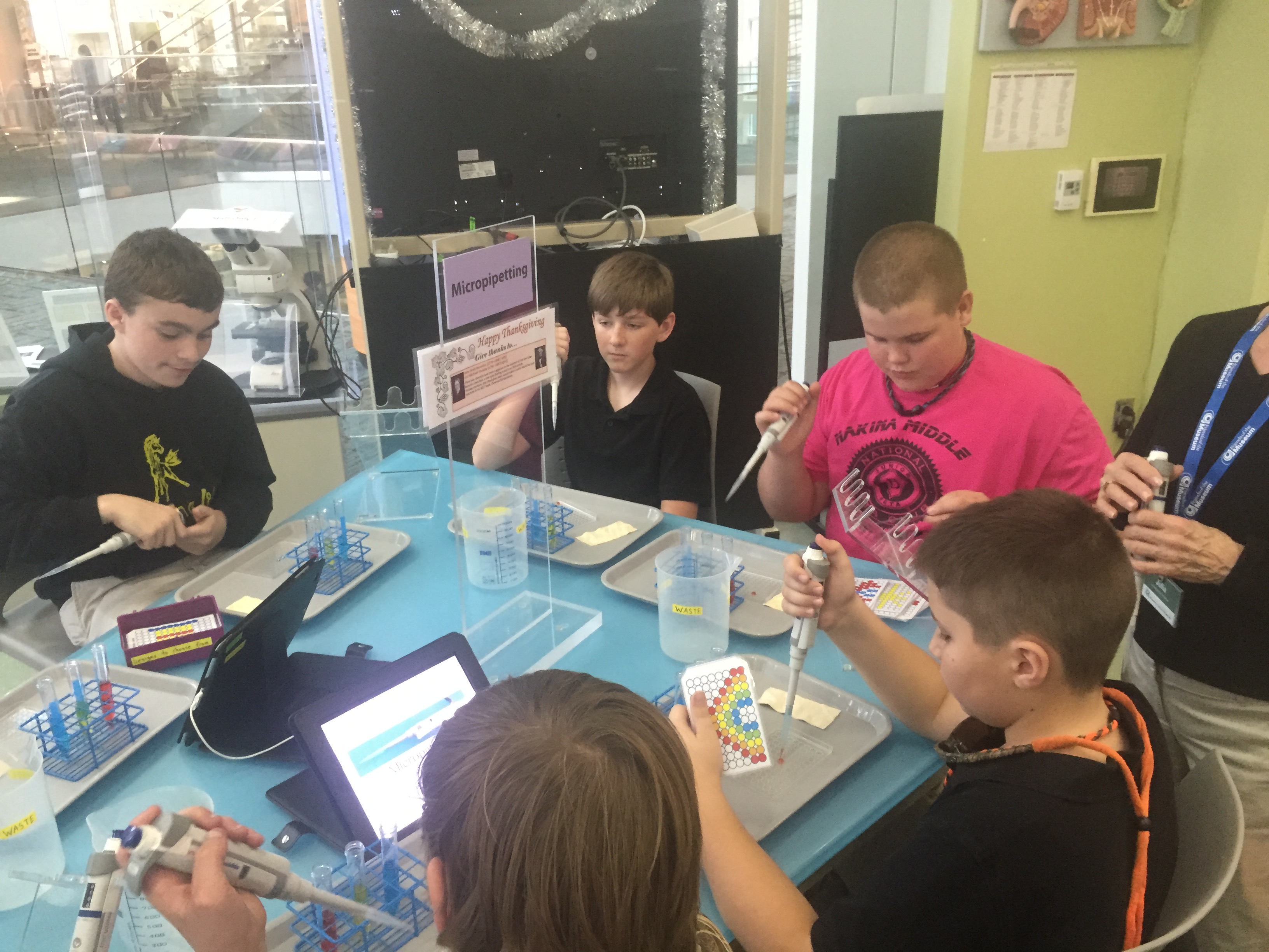 hildren sitting around a table with electronic devices, engaged in technology-based activities.