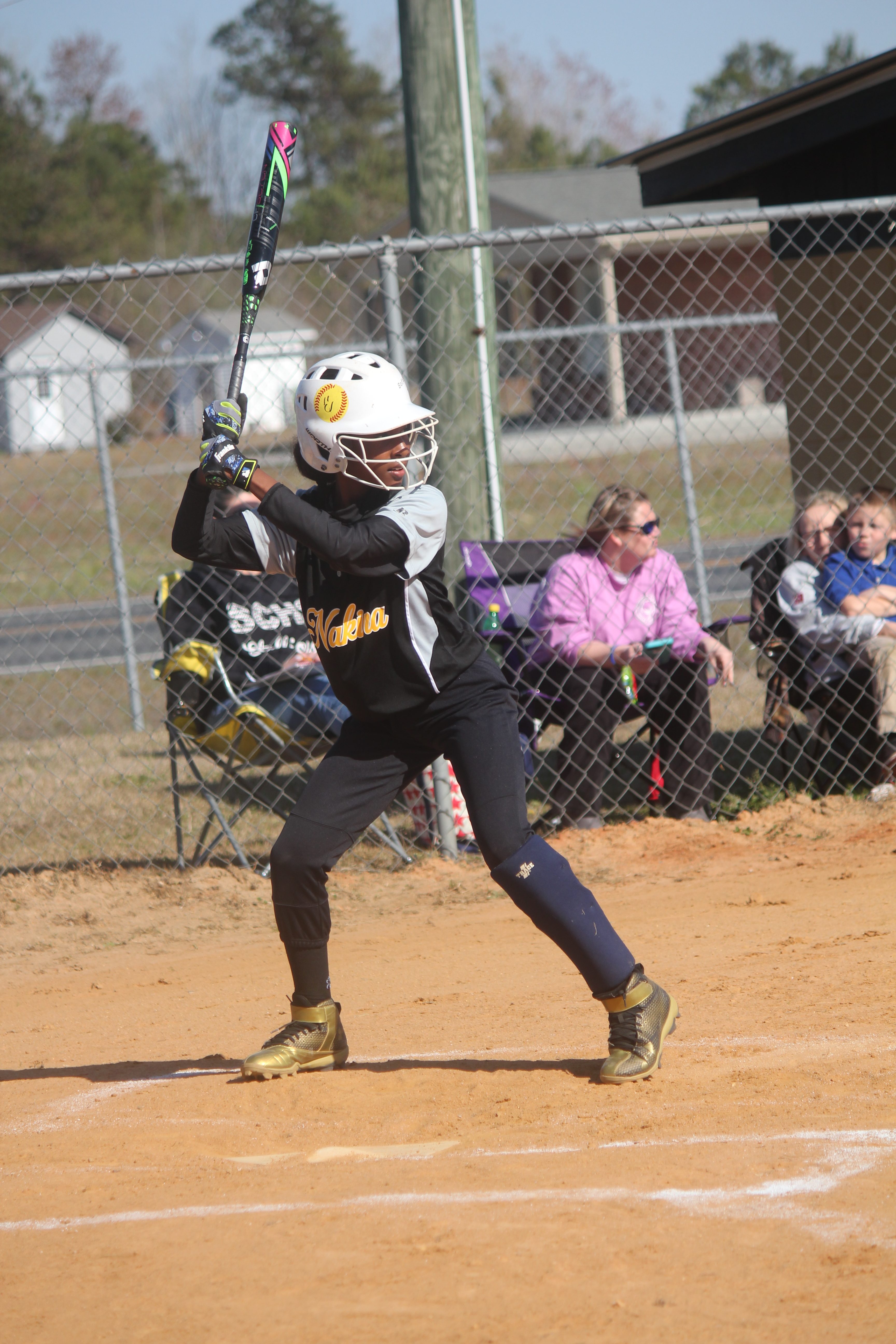 Young girl swinging a bat at a ball during a baseball game.