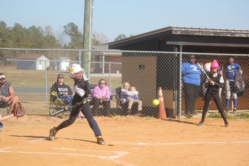 Young girl swinging bat at softball during game.