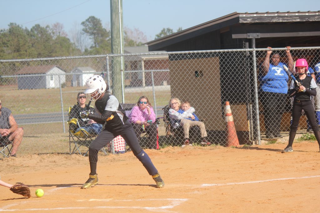 A softball player in action, swinging at a ball during a game.