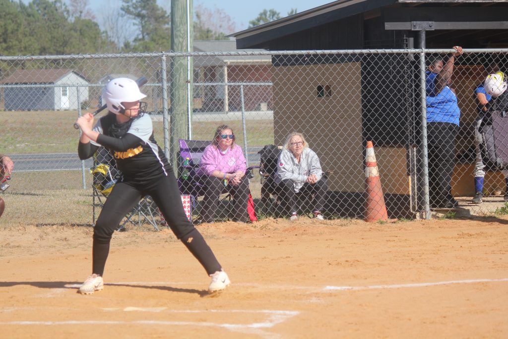 Softball player in black and yellow uniform preparing to swing bat.