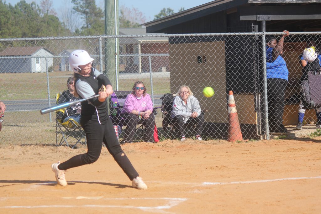 A softball player in action, swinging her bat at a ball during a game.