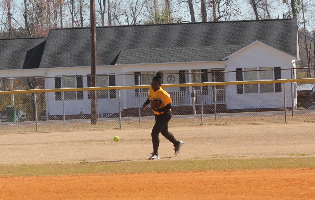 A softball player standing in the outfield, ready to catch the ball on a sunny field.