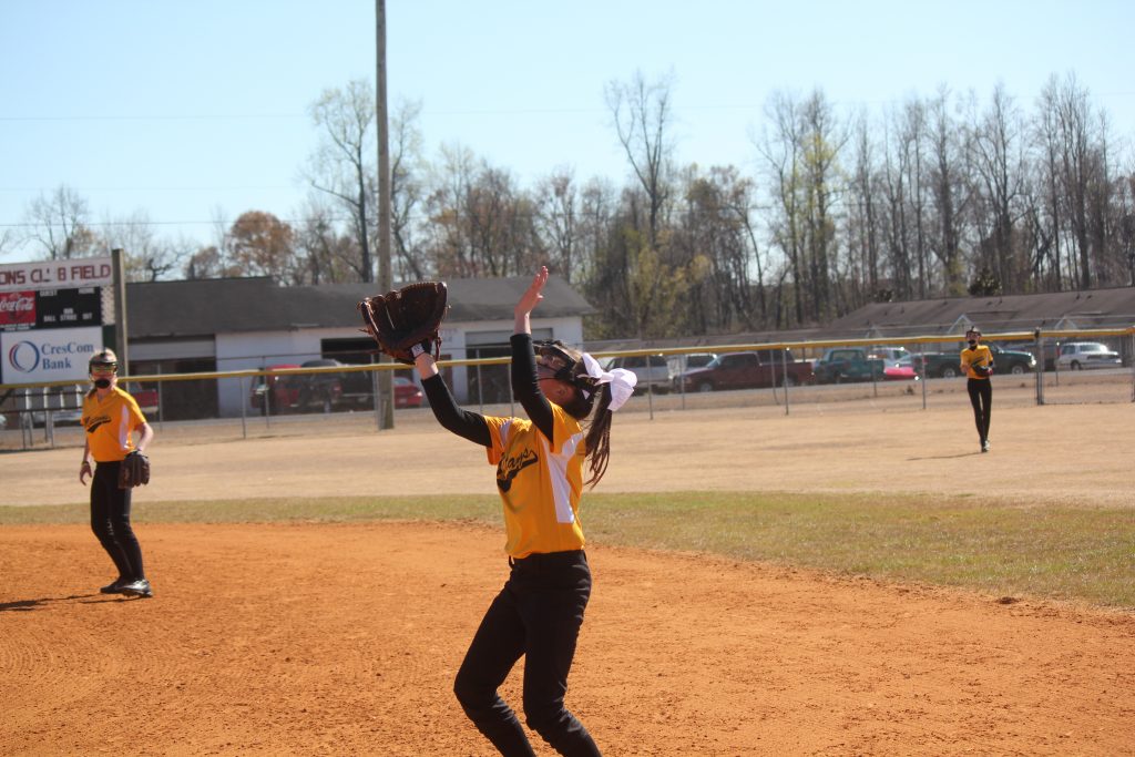 A girl in a yellow and black uniform catching a ball on the field.