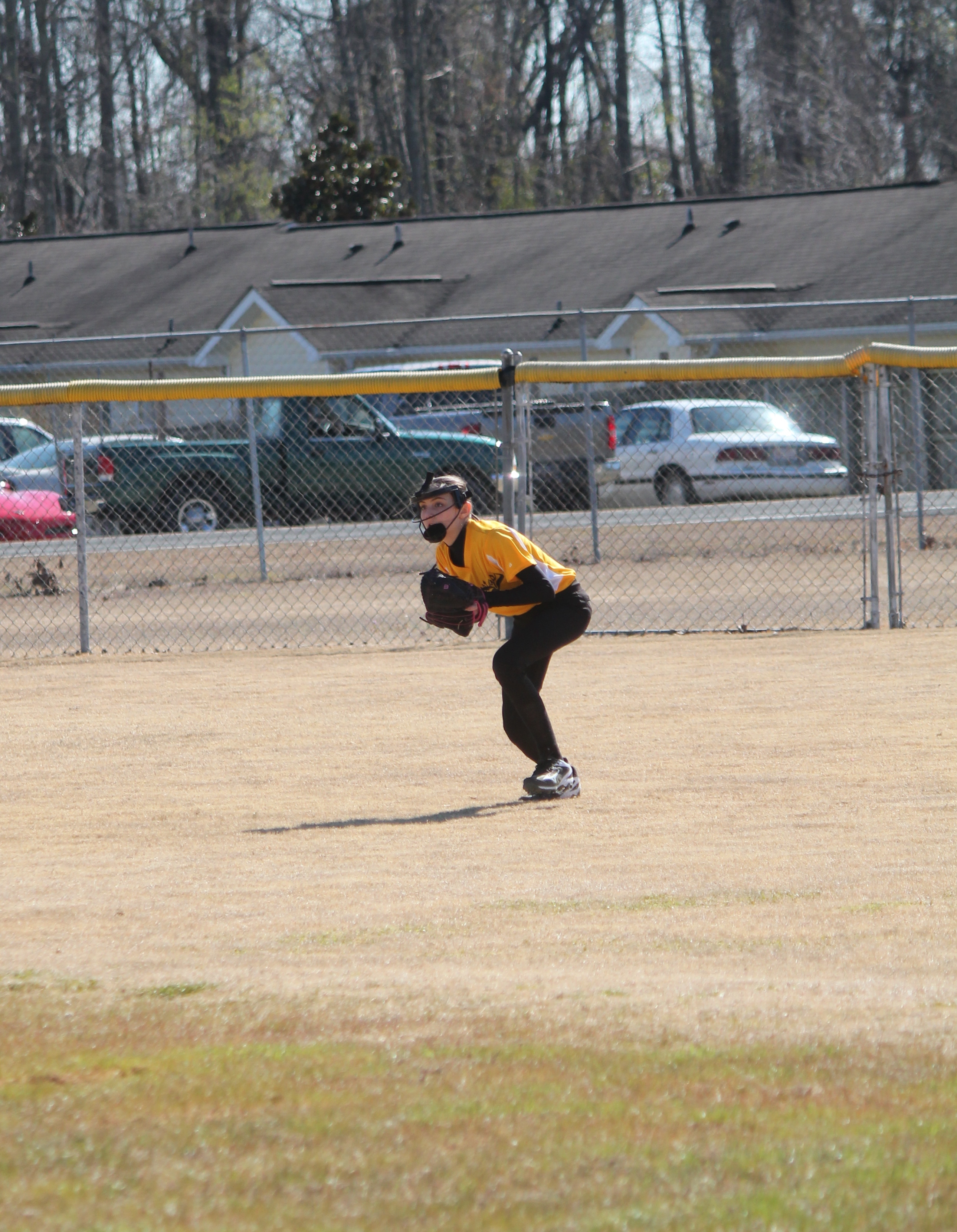 A woman in a yellow and black uniform catching a ball on the field.