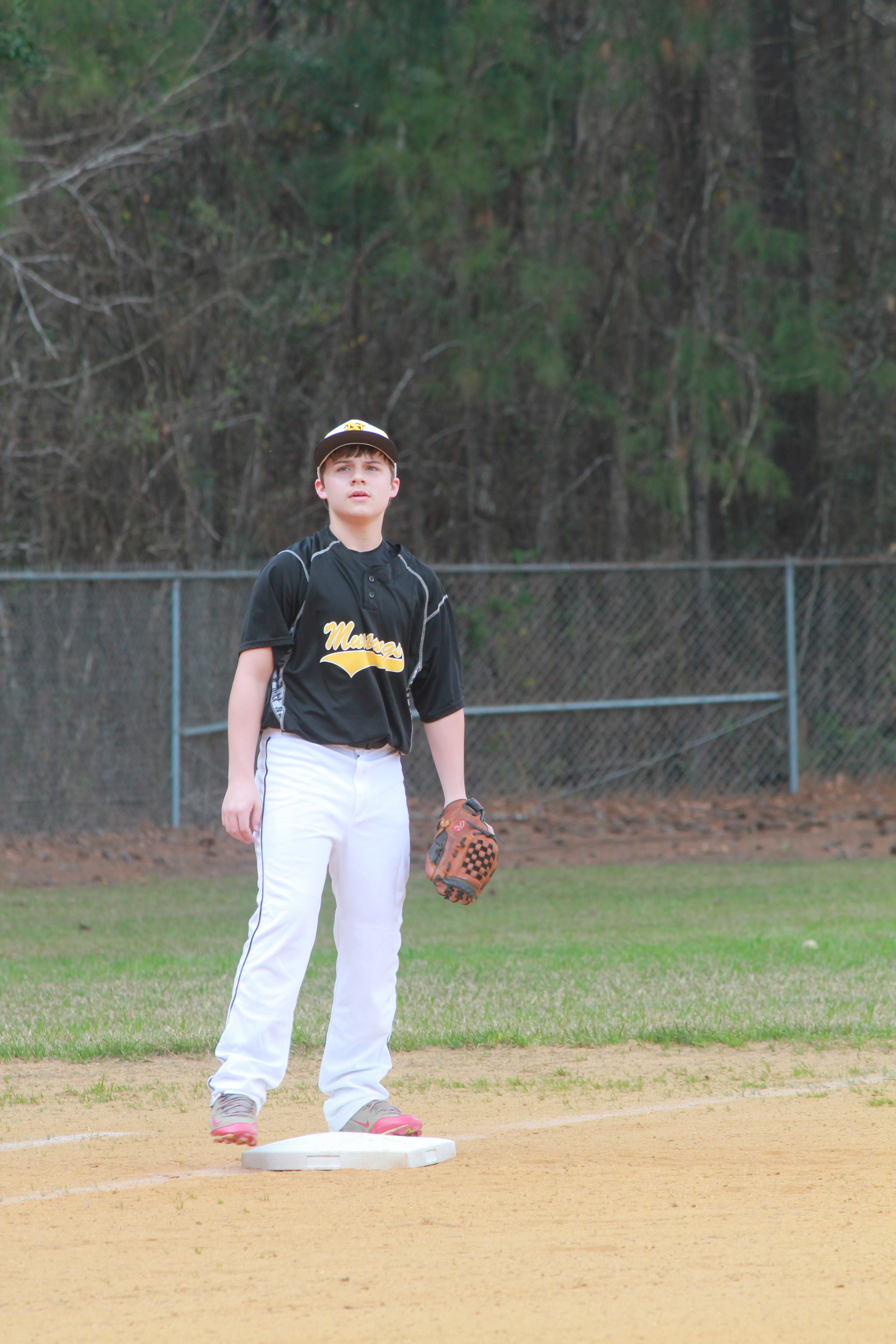 A young boy standing on a baseball field, holding a glove.