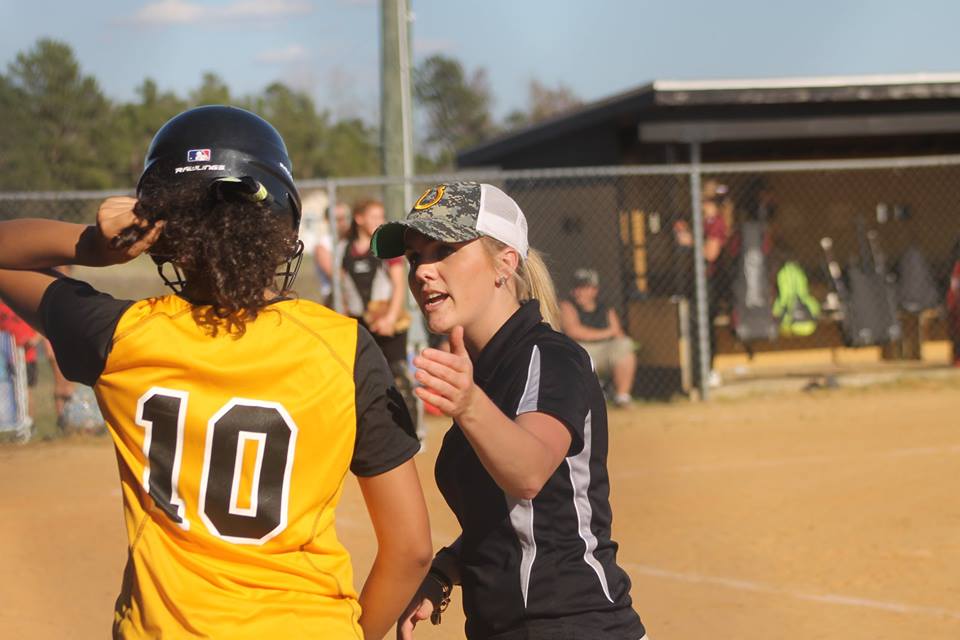 Two female softball players having a conversation on the field during a game.