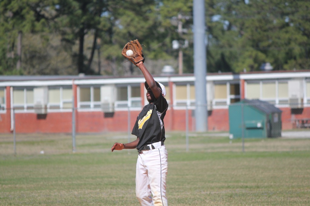 A baseball player in a black uniform catching a ball mid-air during a game.