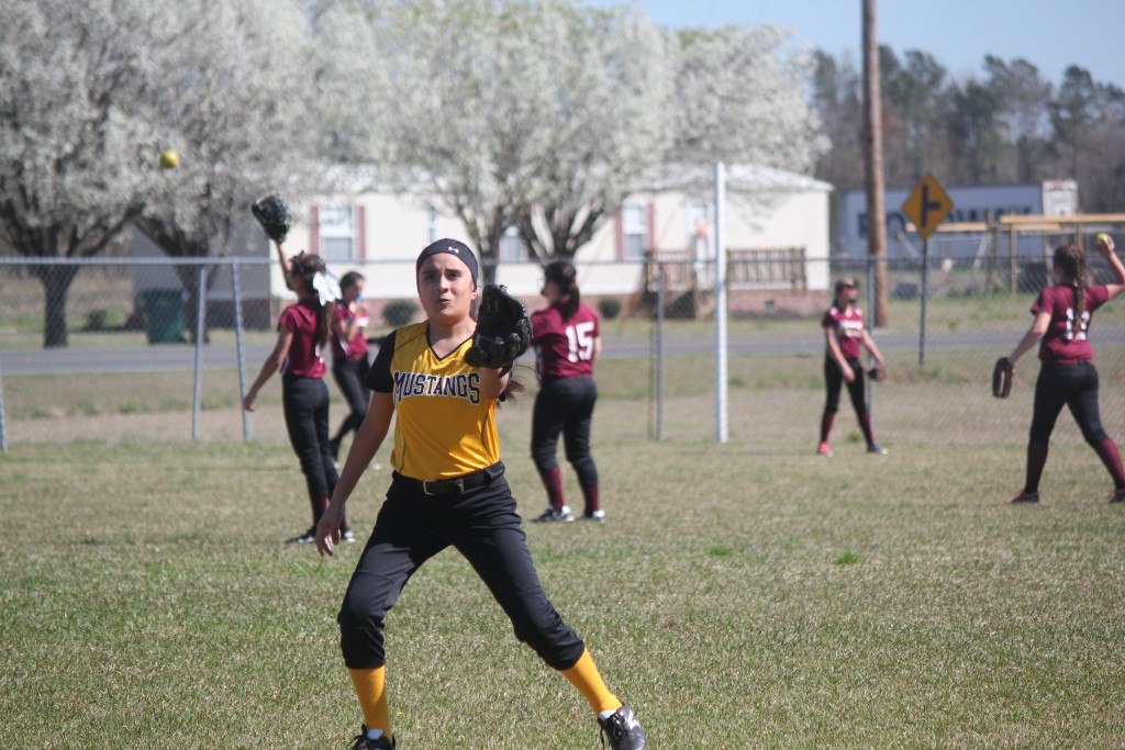 A softball player in a yellow and black uniform, ready to catch a ball.