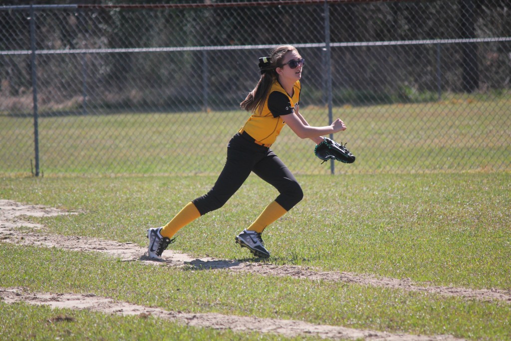 Young female athlete in yellow and black uniform sprinting across a grassy field.