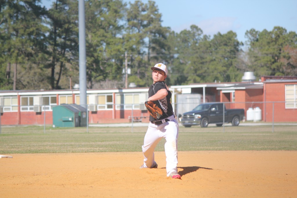 A baseball player in a white uniform pitching a ball on a green field.