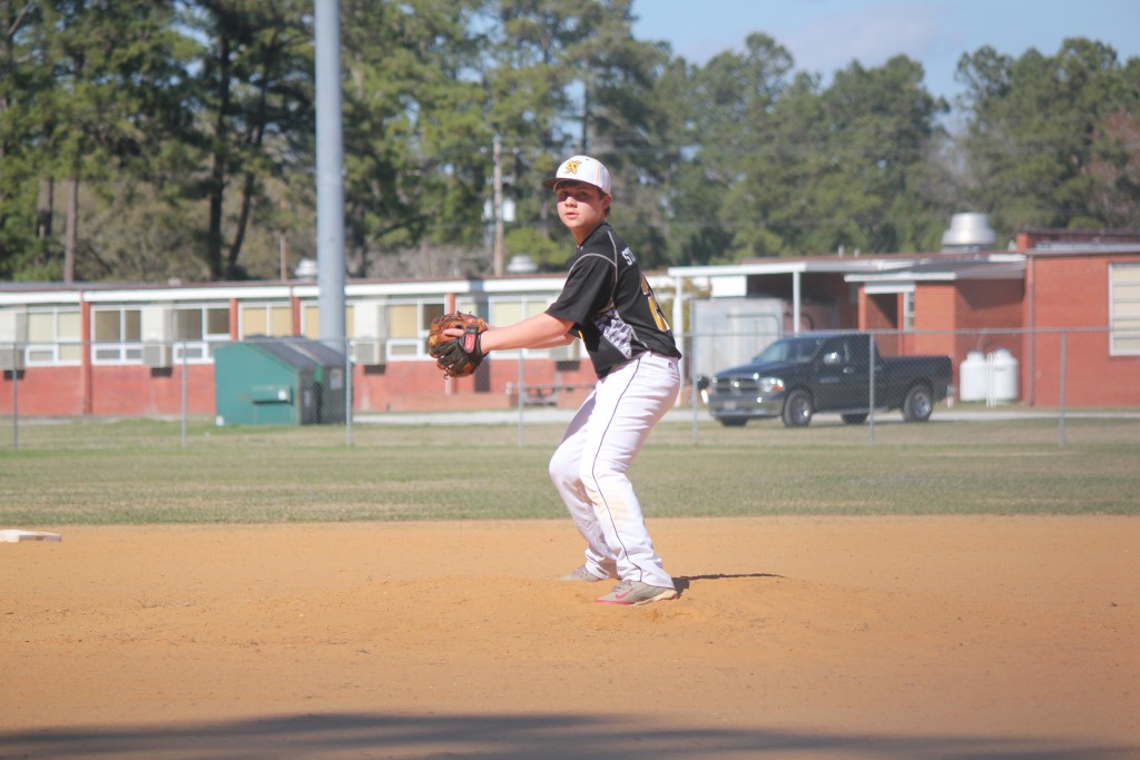 A baseball player in a white uniform pitching a ball on a green field.