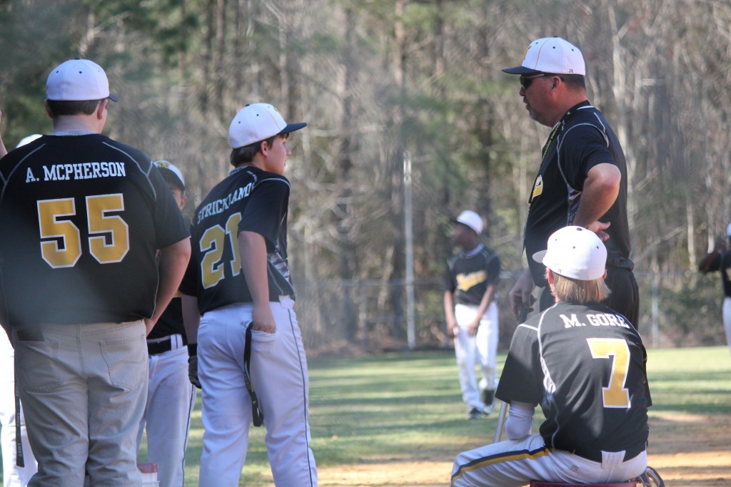 A baseball team huddles around their coach on the field.