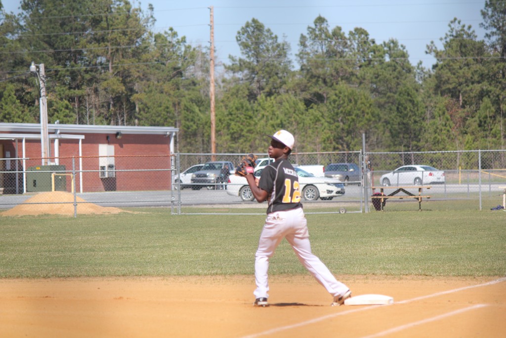 A baseball player in uniform standing on a green field, holding a baseball.