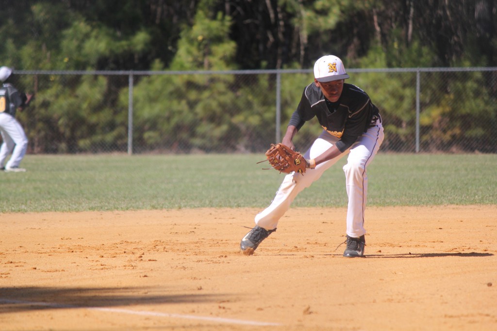 A baseball player in a black and white uniform catching a ball on a sunny day.