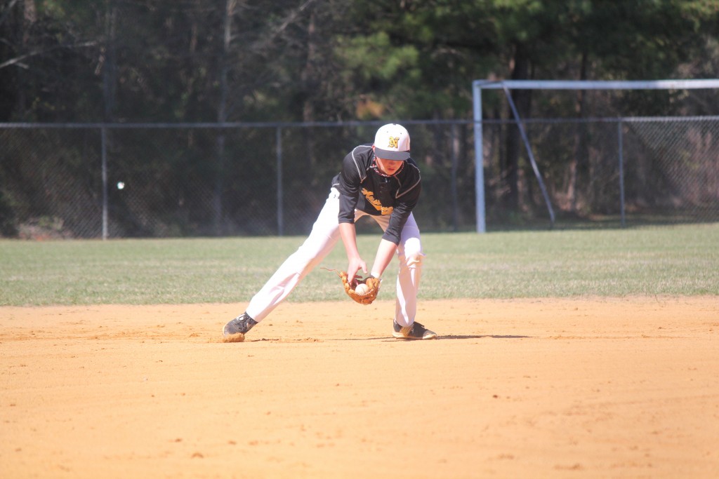 A baseball player in a black and white uniform catching a ball on a sunny day.